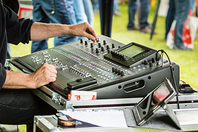 Hands using audio mixing board on outdoors concert.
